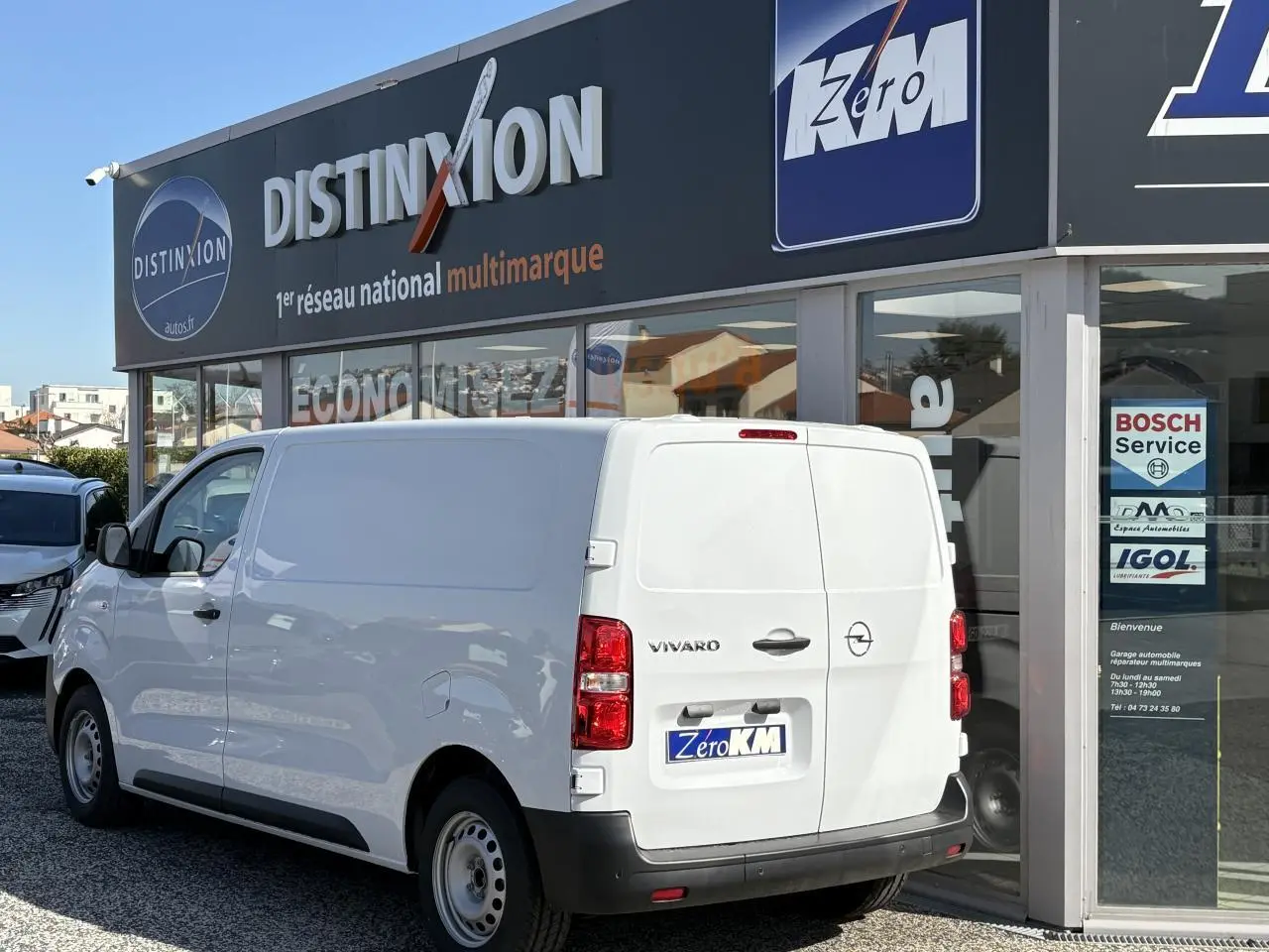 Vue 3/4 arrière droite d’un Opel Vivaro blanc 2024 stationné devant un garage multimarque.
