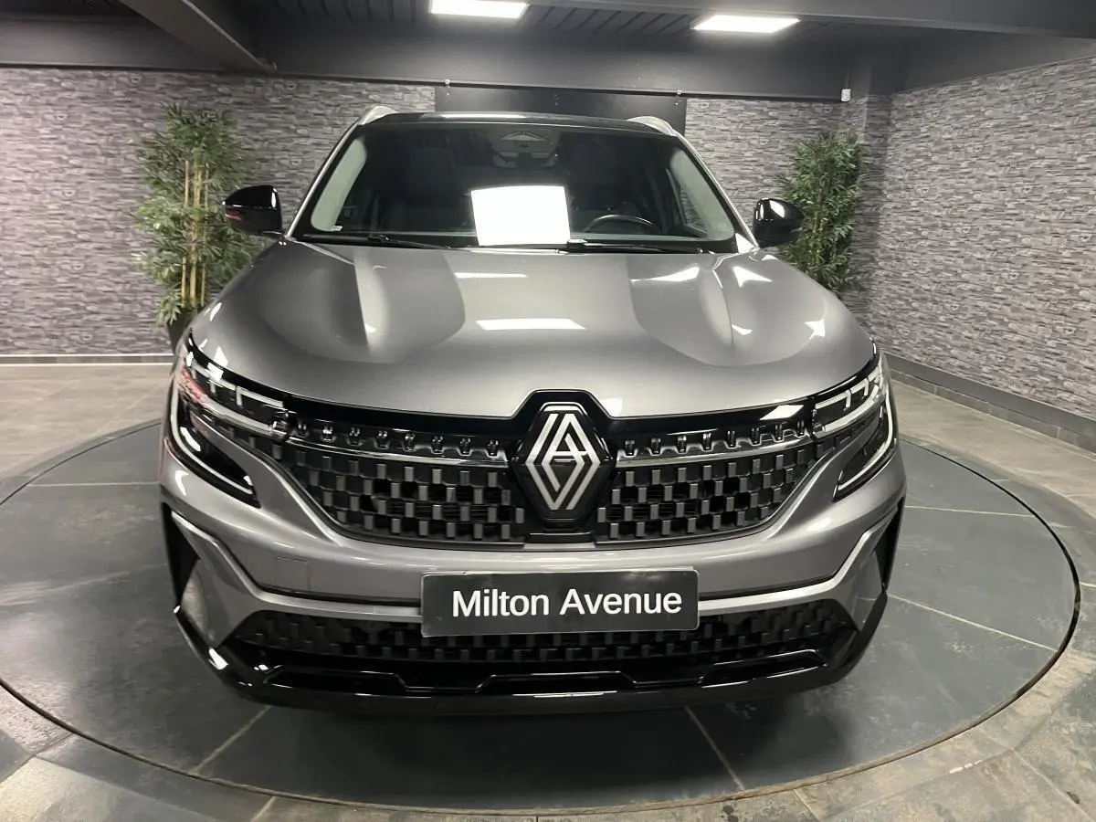 Vue frontale du Renault Austral gris avec calandre damier ice black et logo Renault proéminent, en intérieur showroom.