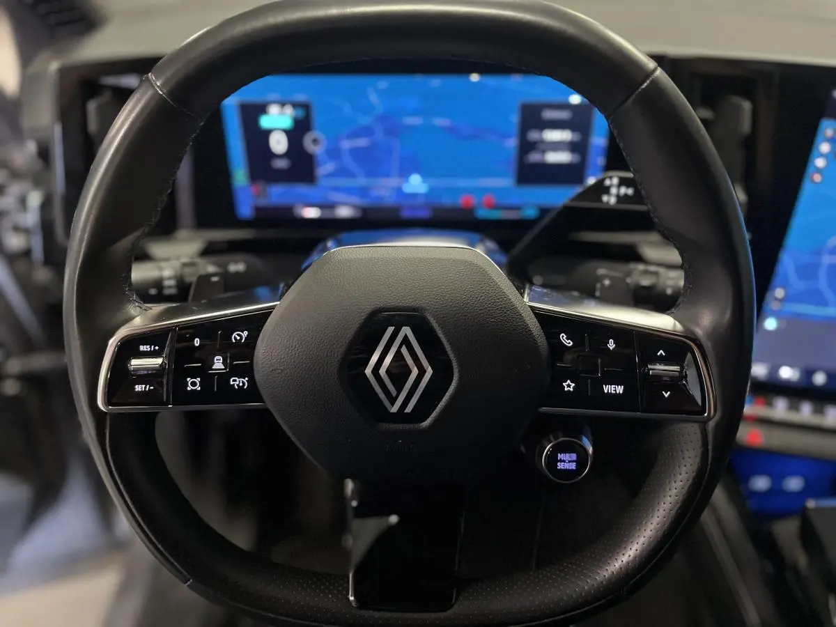 Vue rapprochée du volant noir de Renault Austral 2024 avec commandes intégrées et tableau de bord numérique lumineux en arrière-plan