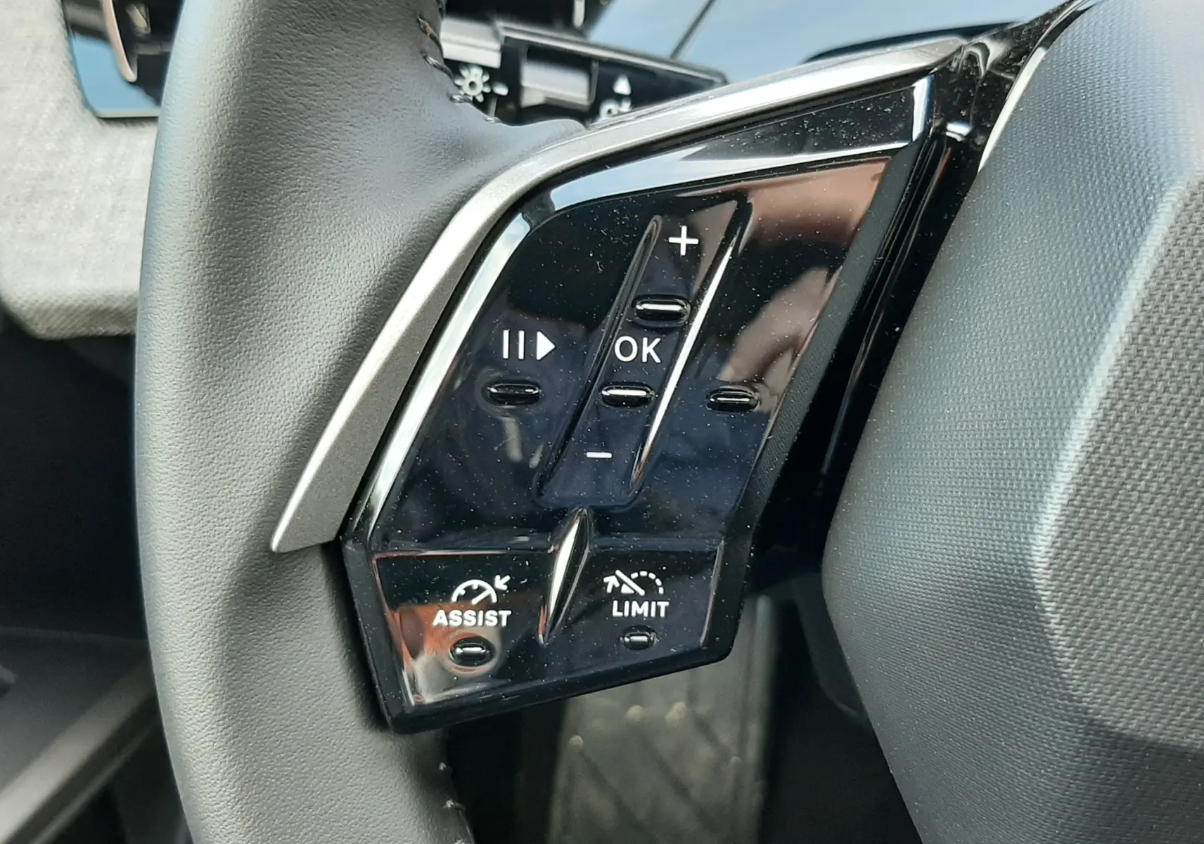 Gros plan sur les commandes noires du volant côté gauche du Peugeot 5008 bleu Ingaro, version hybride 2025.