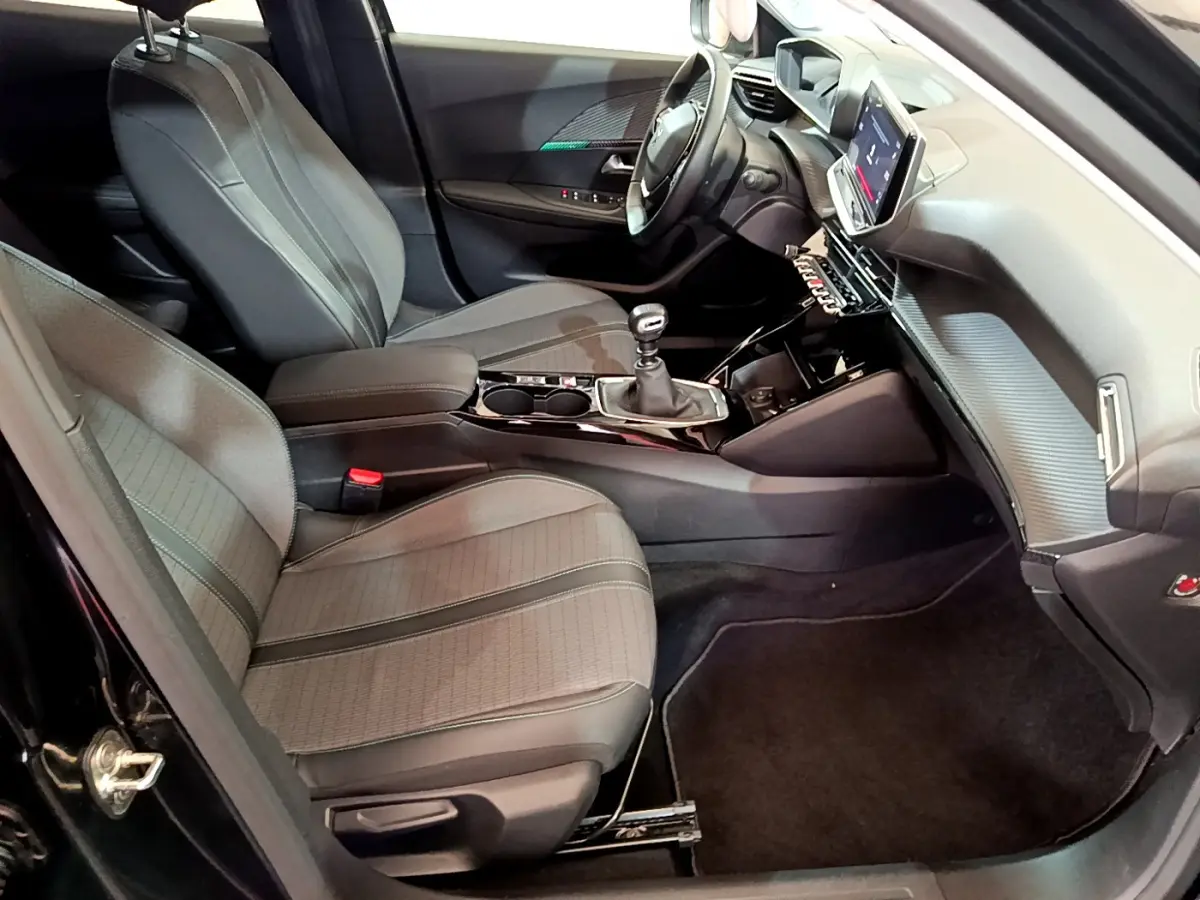 Intérieur avant droit du Peugeot 2008 noir 2021, sièges tissu, tableau de bord avec écran tactile et boîte manuelle.