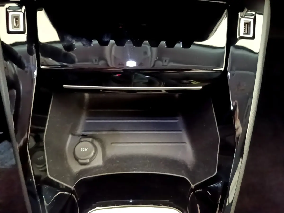 Gros plan sur la console centrale noire du Peugeot 2008 avec prise 12V et finition brillante autour.