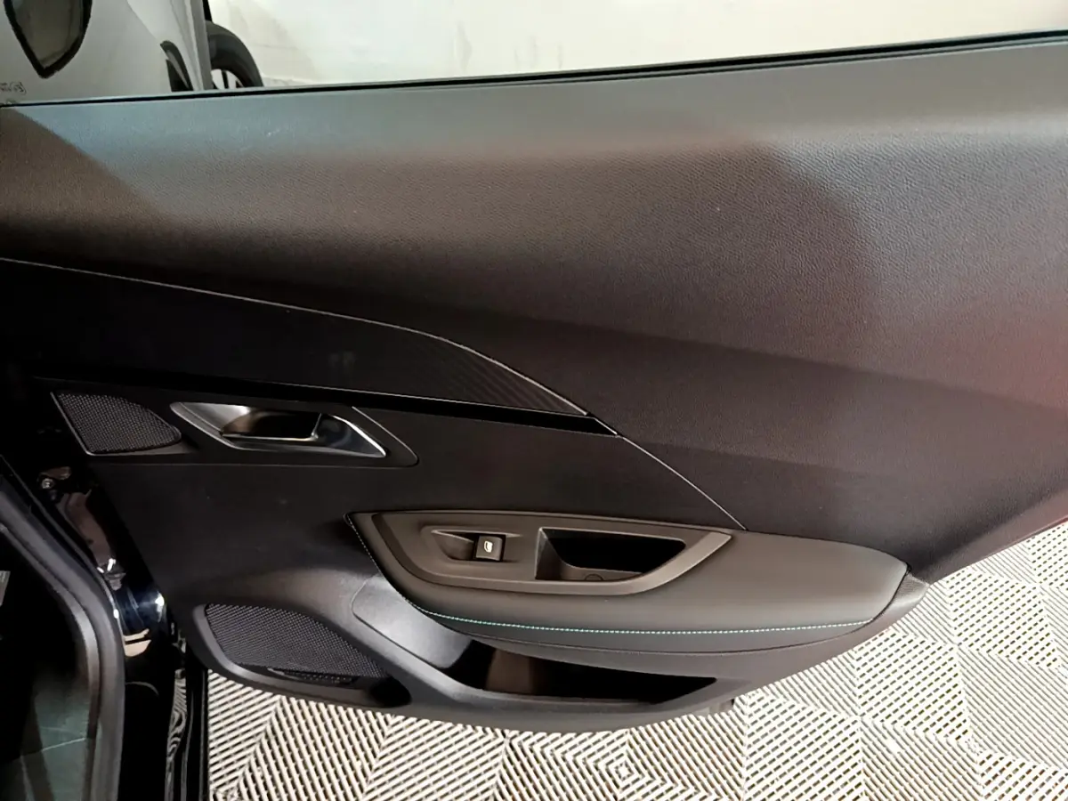 Intérieur côté gauche de la porte d'une Peugeot 2008 noire, avec garniture noire et surpiqûres bleues.