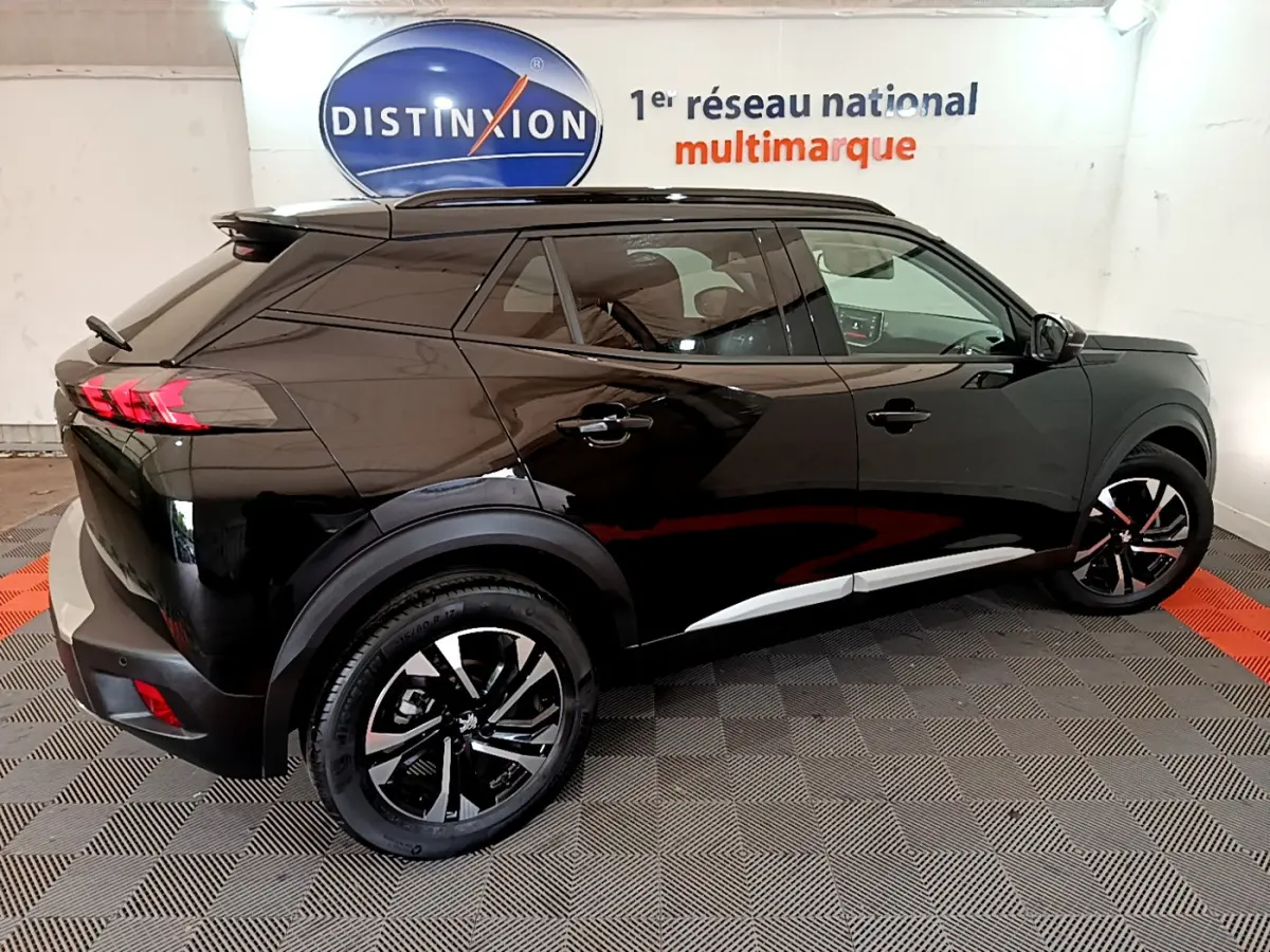 Vue 3/4 arrière droite d'un Peugeot 2008 noir 2021 avec jantes noires et toit noir brillant dans un showroom.