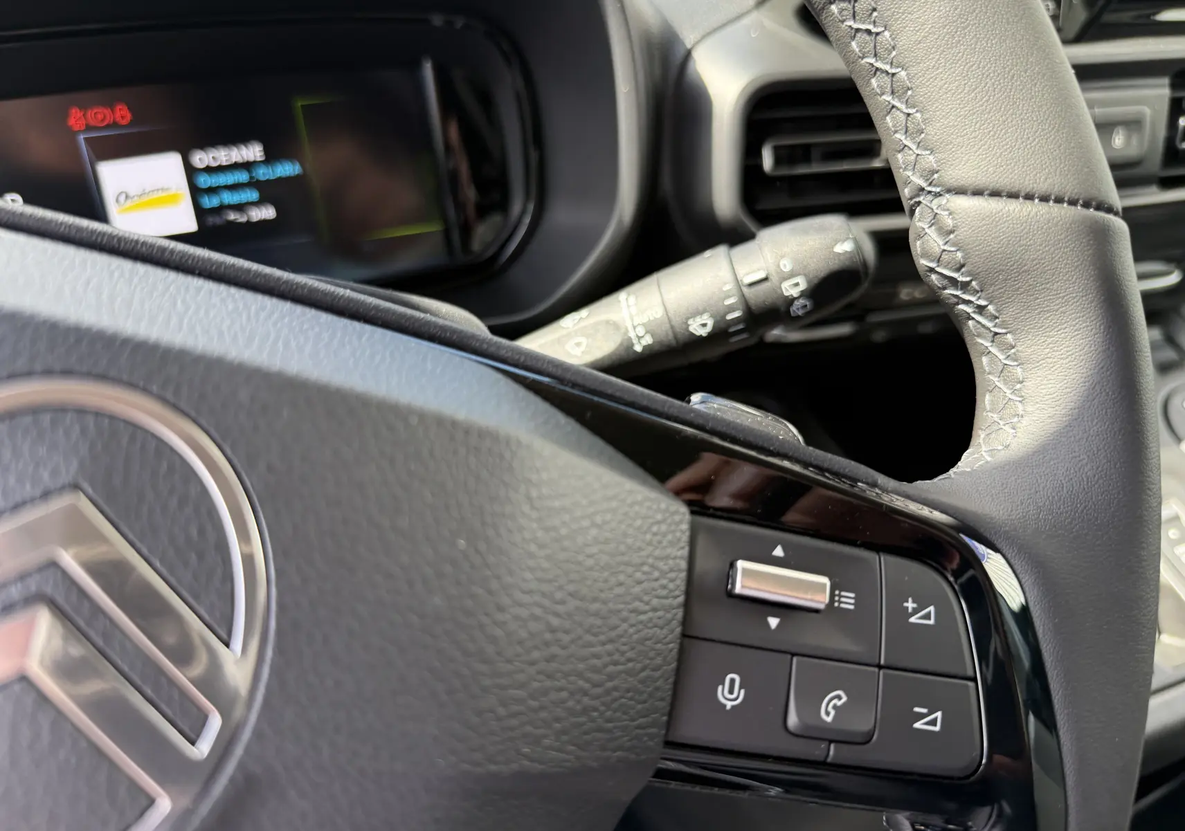 Gros plan sur le volant cuir gris du Citroën Berlingo 2026 avec commandes multifonctions et tableau de bord numérique partiel.
