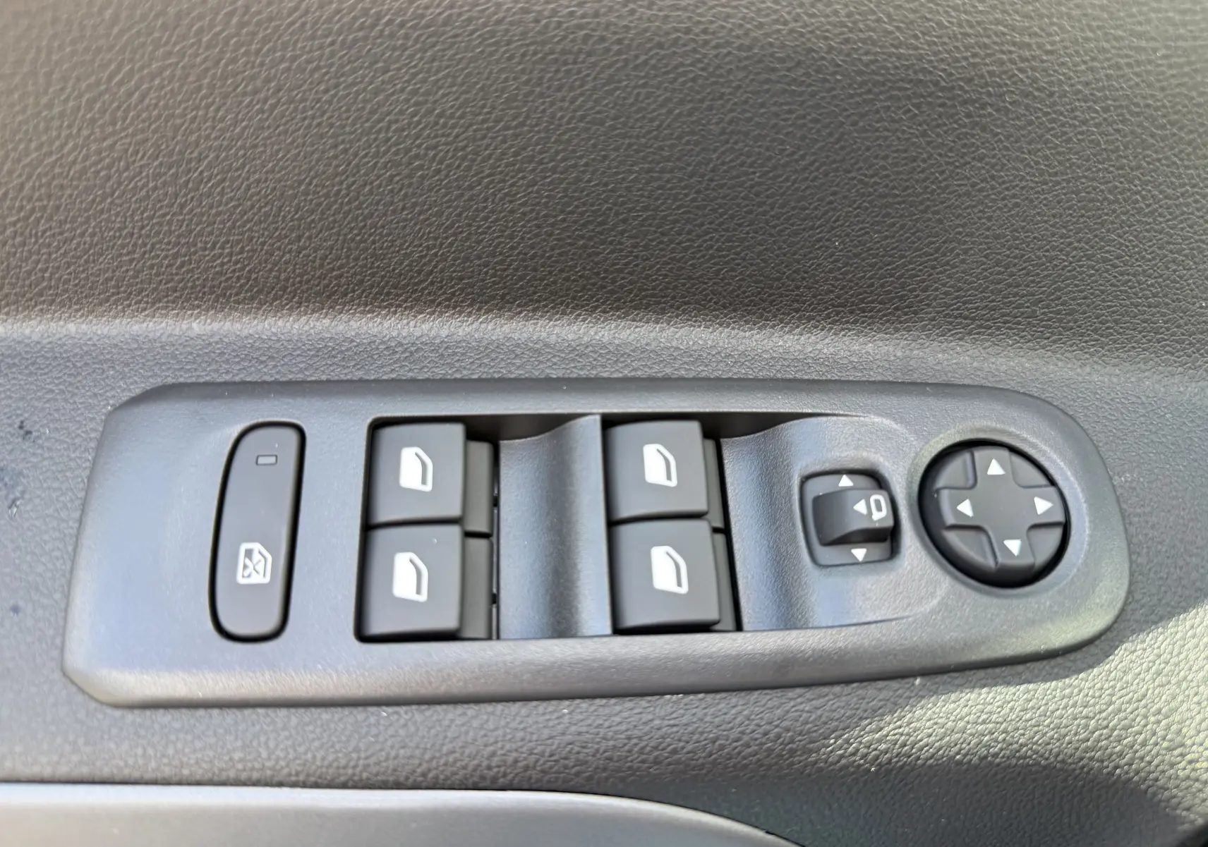Panneau de commandes des vitres et rétroviseurs côté conducteur du Citroën Berlingo gris Artense, vue rapprochée intérieure.
