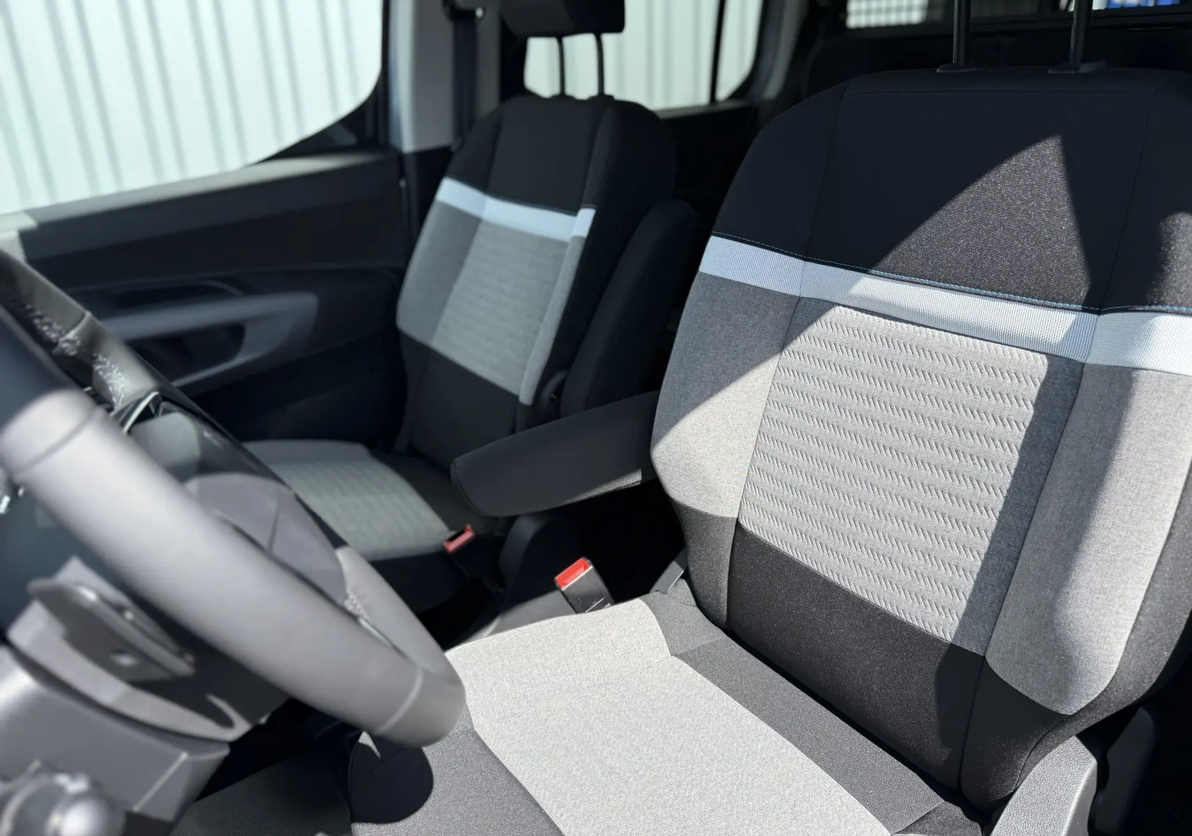 Vue intérieure rapprochée des sièges avant gris clair et noir du Citroën Berlingo 2026, avec accoudoir côté droit.
