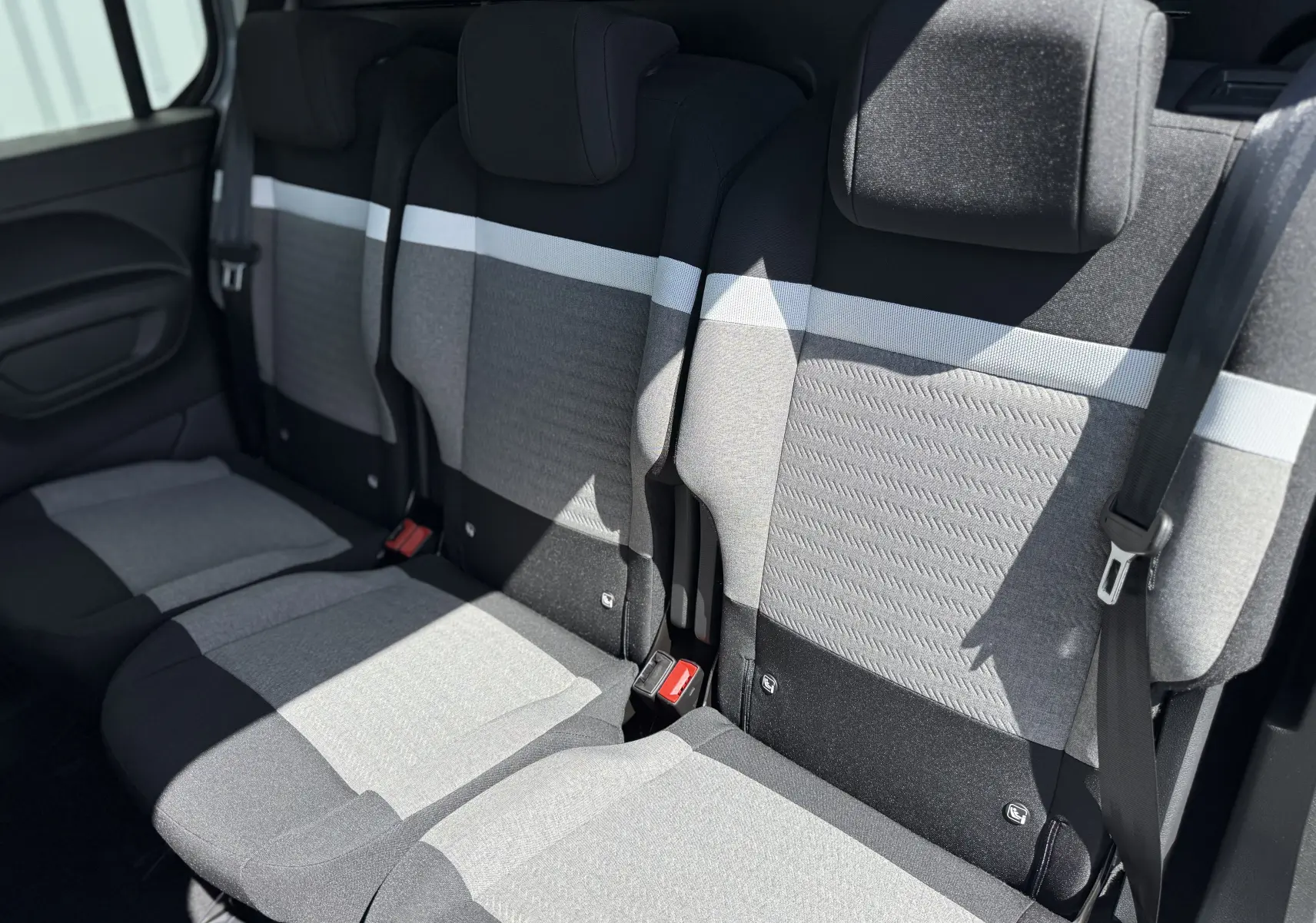 Vue intérieure des sièges arrière du Citroën Berlingo 2026, tissu gris clair et noir avec ceinture de sécurité visible.