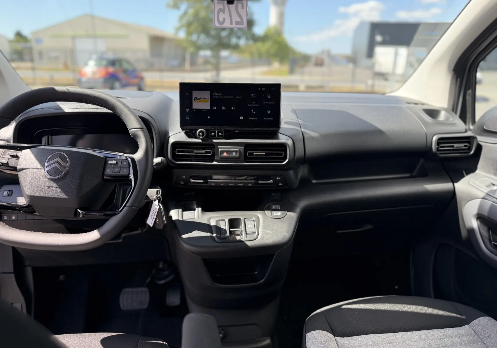 Vue intérieure avant du Citroën Berlingo gris Artense, tableau de bord moderne avec écran tactile central et volant multifonction.