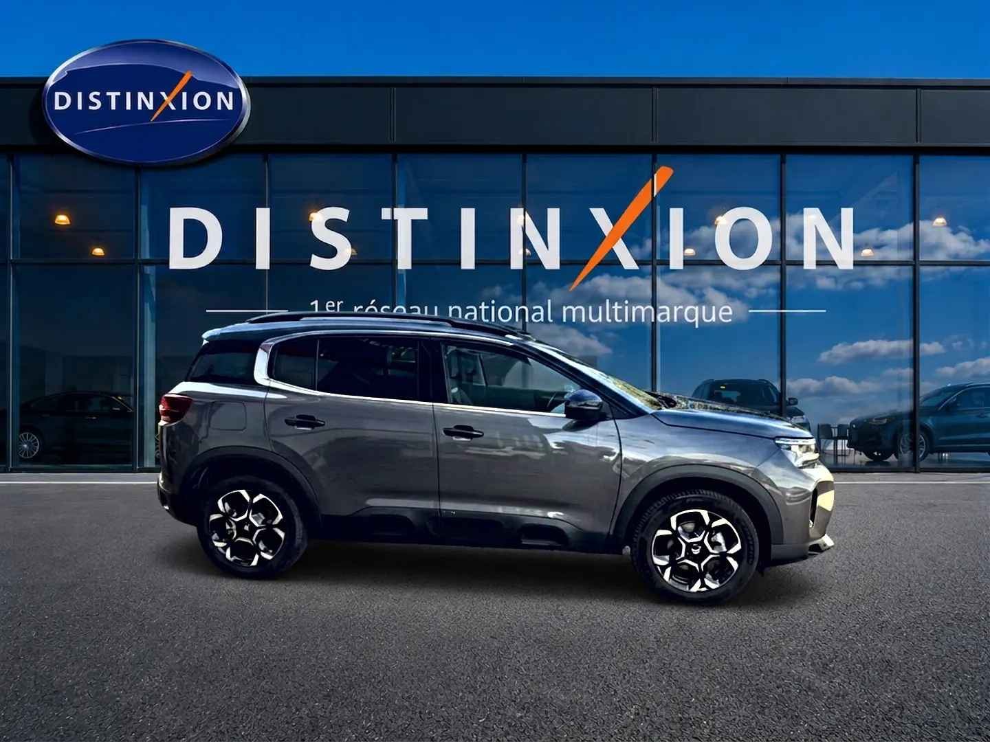 Profil droit du Citroën C5 Aircross gris 2025 avec jantes alu et barres de toit devant vitrine Distinxion.