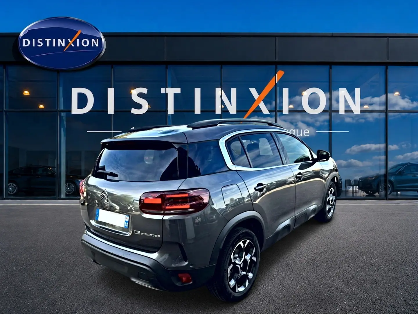 Vue 3/4 arrière droite d'un Citroën C5 Aircross gris 2025 avec jantes alu et vitres arrière teintées, devant un showroom.
