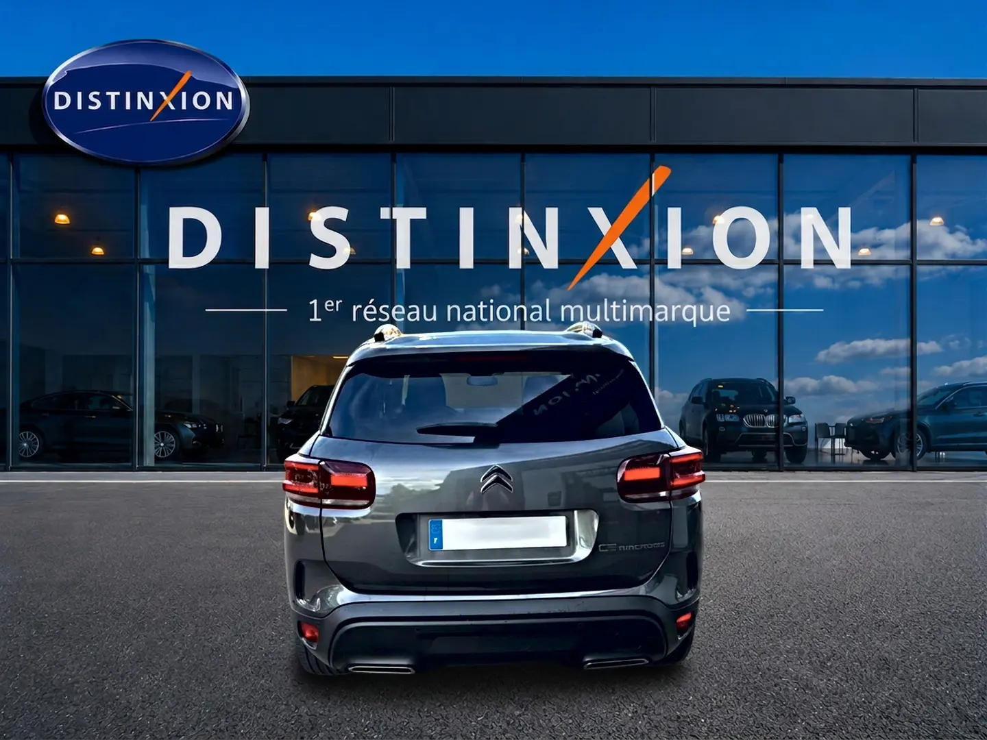 Vue arrière d'un Citroën C5 Aircross gris 2025 stationné devant une vitrine avec logo Distinxion.