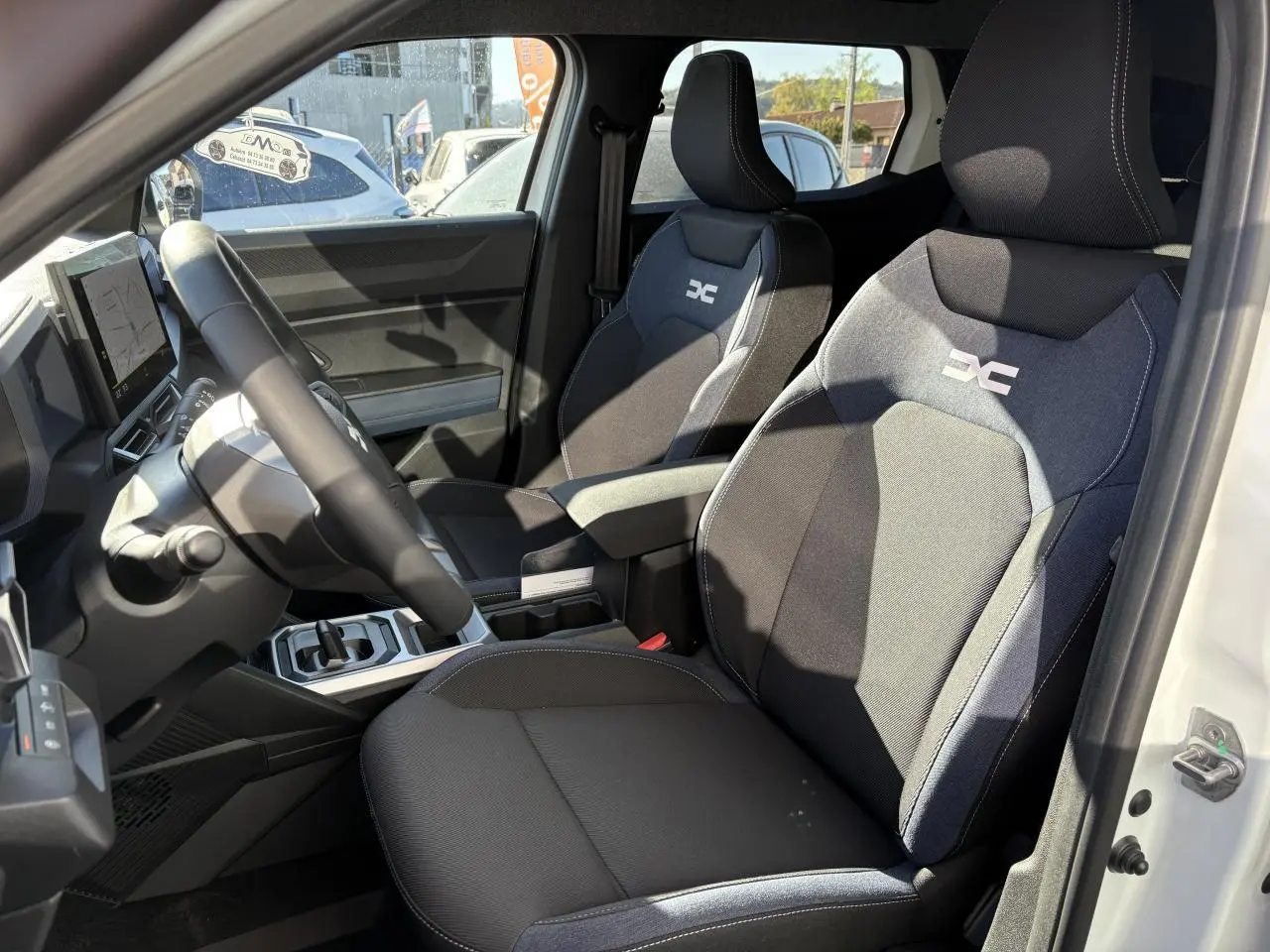 Intérieur du Dacia Duster 2024 vu côté conducteur, sièges tissu Denim bleu avec logo Dacia Hybrid brodé.