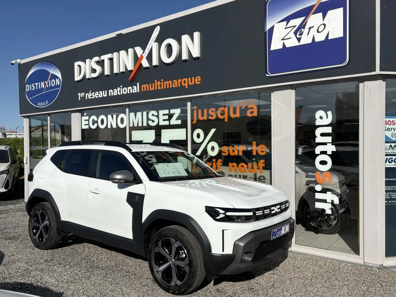 Dacia Duster blanc métallisé en 3/4 avant droit, avec barres de toit noires et jantes alliage 18 pouces.