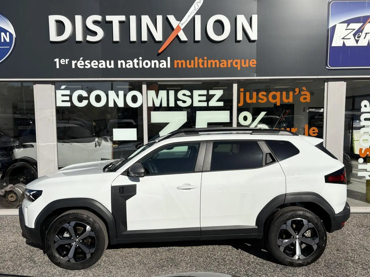 Profil droit du Dacia Duster 2024 blanc métallisé avec jantes alliage noires et barres de toit noires.