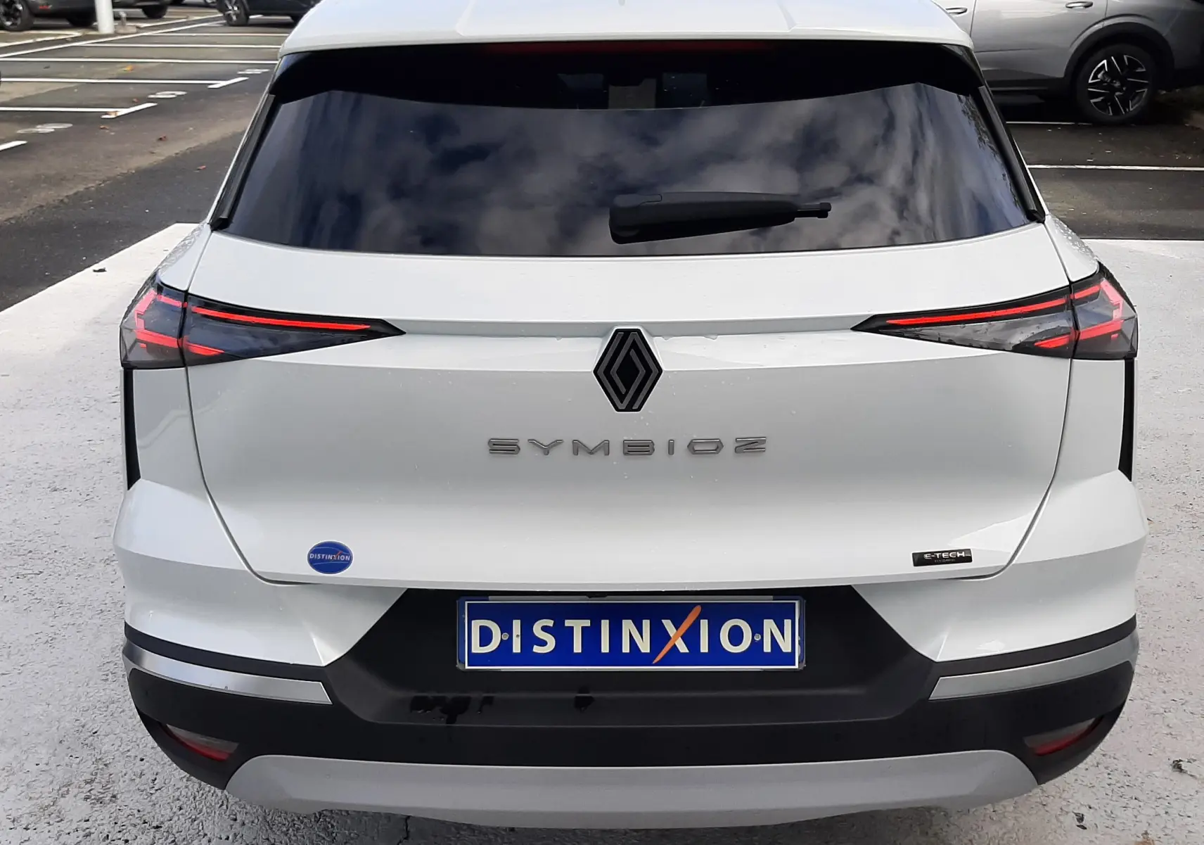 Vue arrière d'une Renault Symbioz blanc nacré, avec feux arrière LED fins et logo central noir brillant.