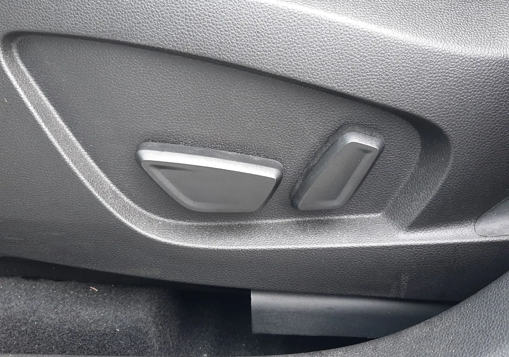 Gros plan sur les commandes électriques de réglage du siège côté gauche dans l’habitacle noir du Renault Symbioz blanc nacré.