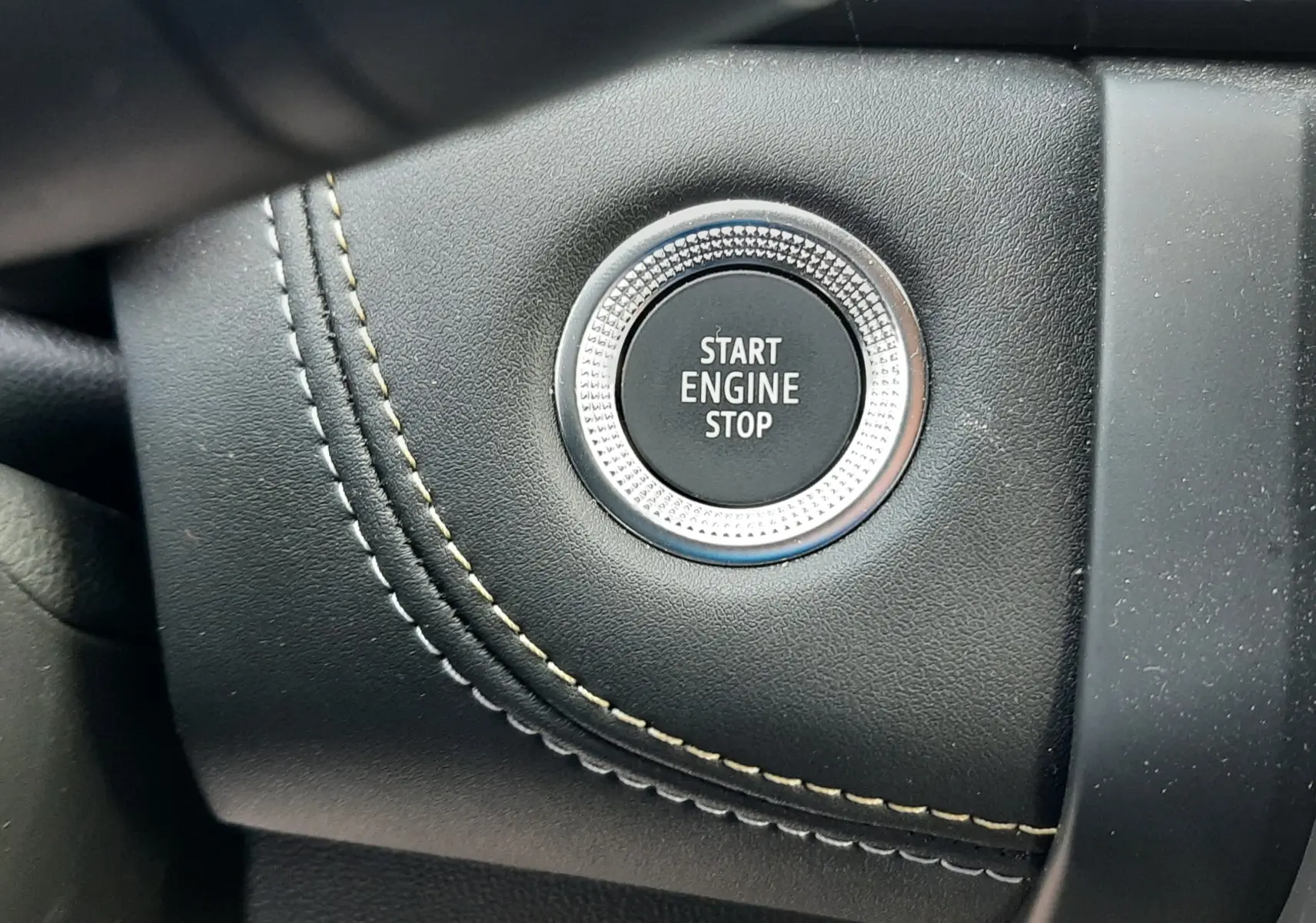 Gros plan sur le bouton Start Engine Stop entouré de cuir noir avec surpiqûres beiges dans la Renault Symbioz hybride 2025.
