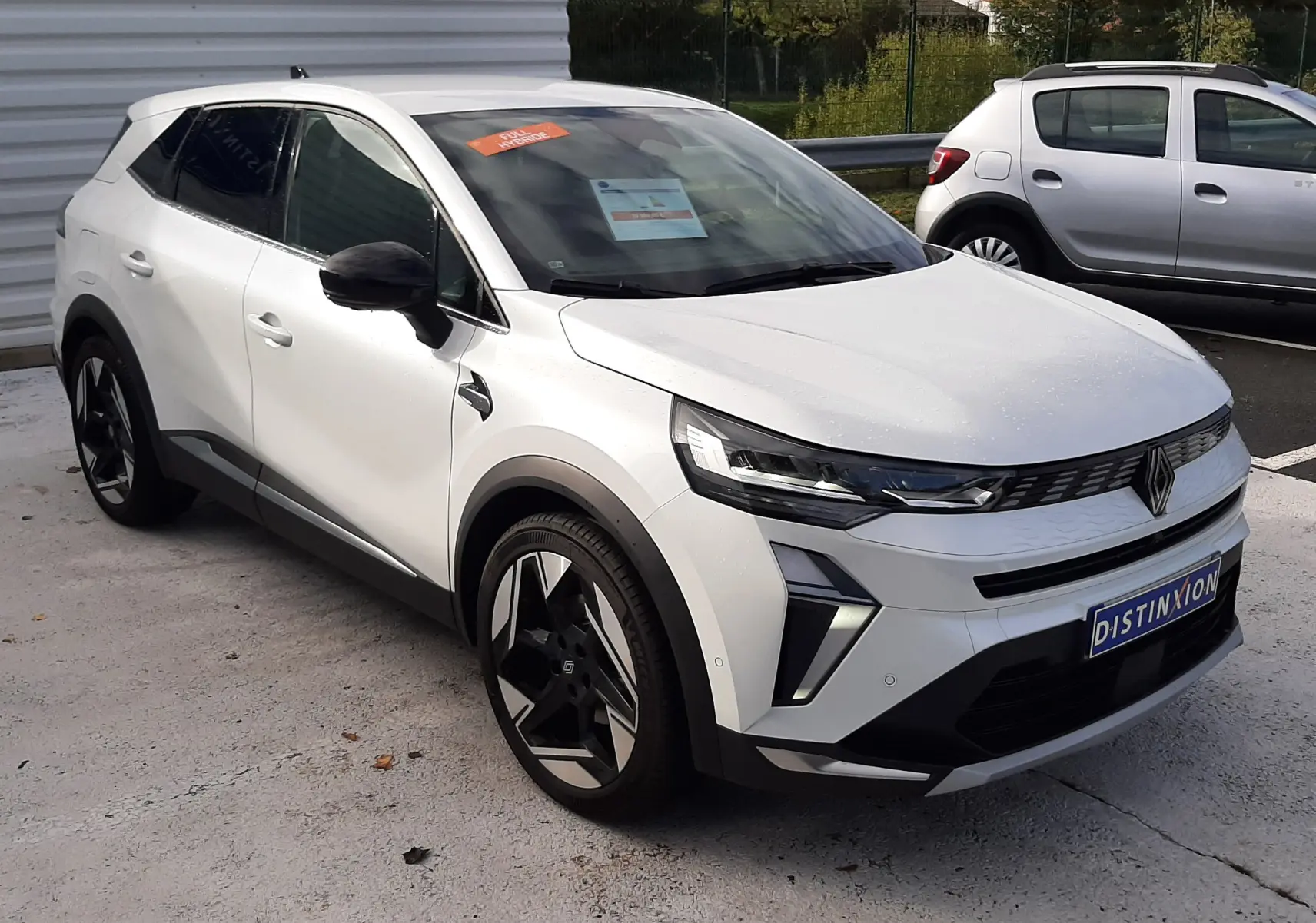 Renault Symbioz blanc nacré en 3/4 avant droit, avec jantes noires et détails noirs contrastants sur les rétroviseurs et bas de caisse.
