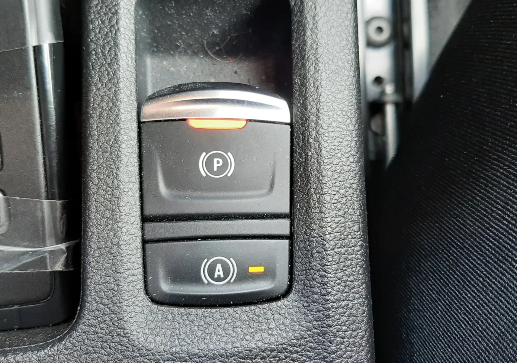 Gros plan sur les commandes de frein à main électronique et arrêt auto dans l’habitacle noir du Renault Symbioz blanc nacré.