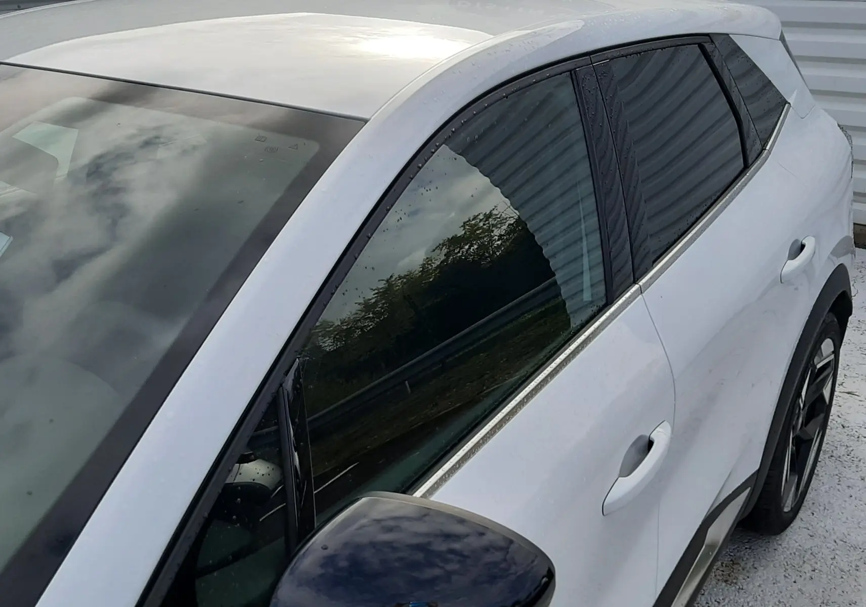 Vue rapprochée côté gauche avant du Renault Symbioz blanc nacré avec rétroviseur noir brillant et vitres teintées.