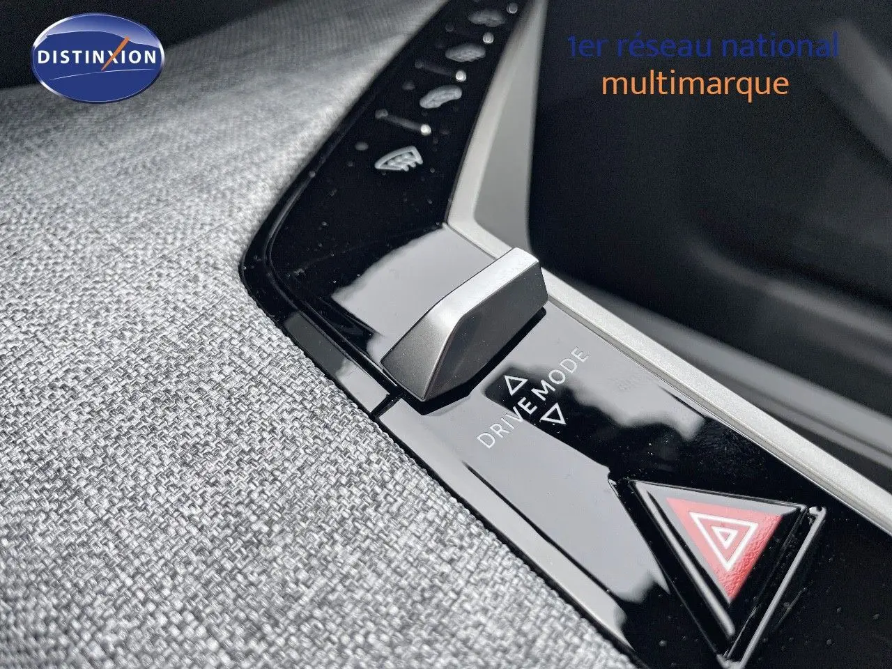Gros plan sur la molette Drive Mode et le bouton de warning sur la console centrale tissu gris du Peugeot 5008 hybride 2025.