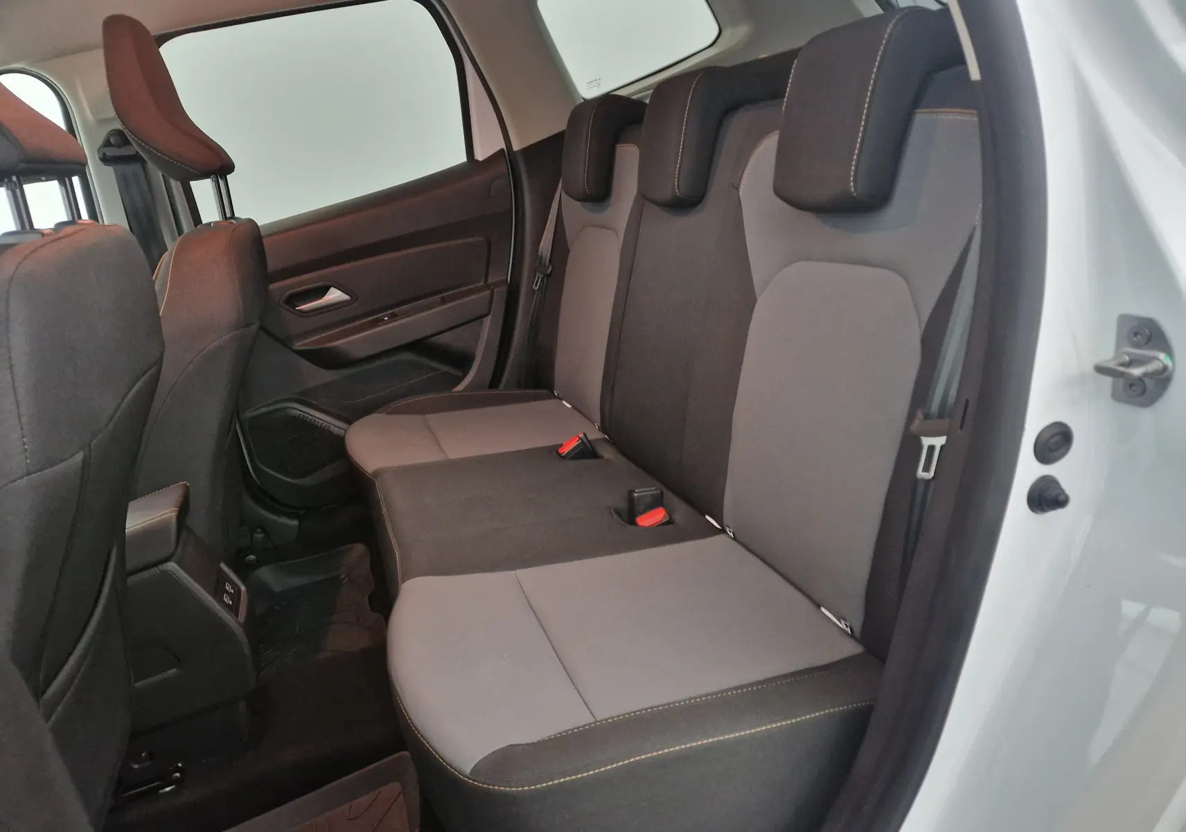 Vue intérieure côté droit sur les sièges arrière gris et noirs du Dacia Duster 4x4 blanc 2024 avec porte ouverte.