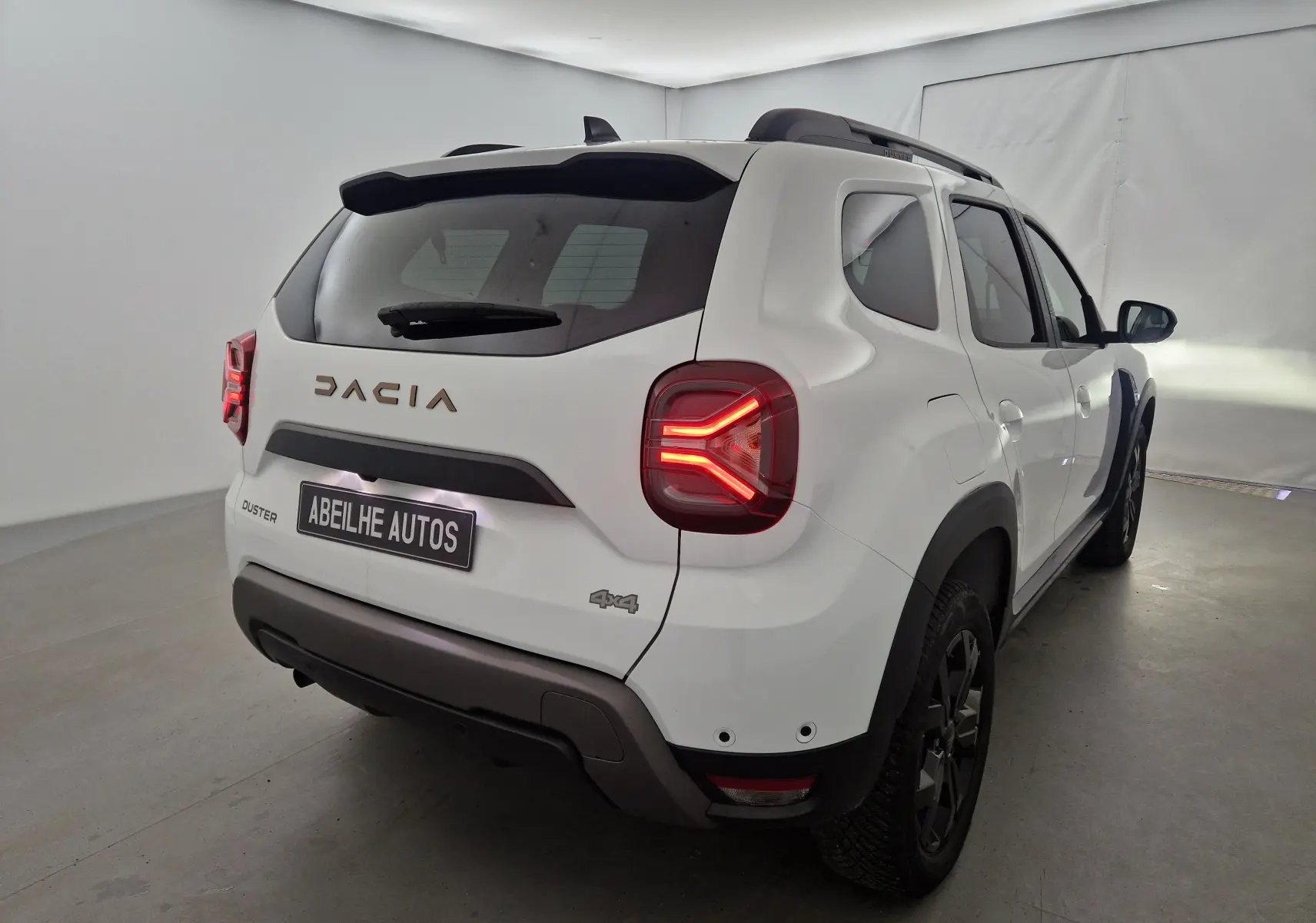 Vue 3/4 arrière droite du Dacia Duster blanc 4x4 2024 avec feux arrière allumés et badge 4x4 visible.