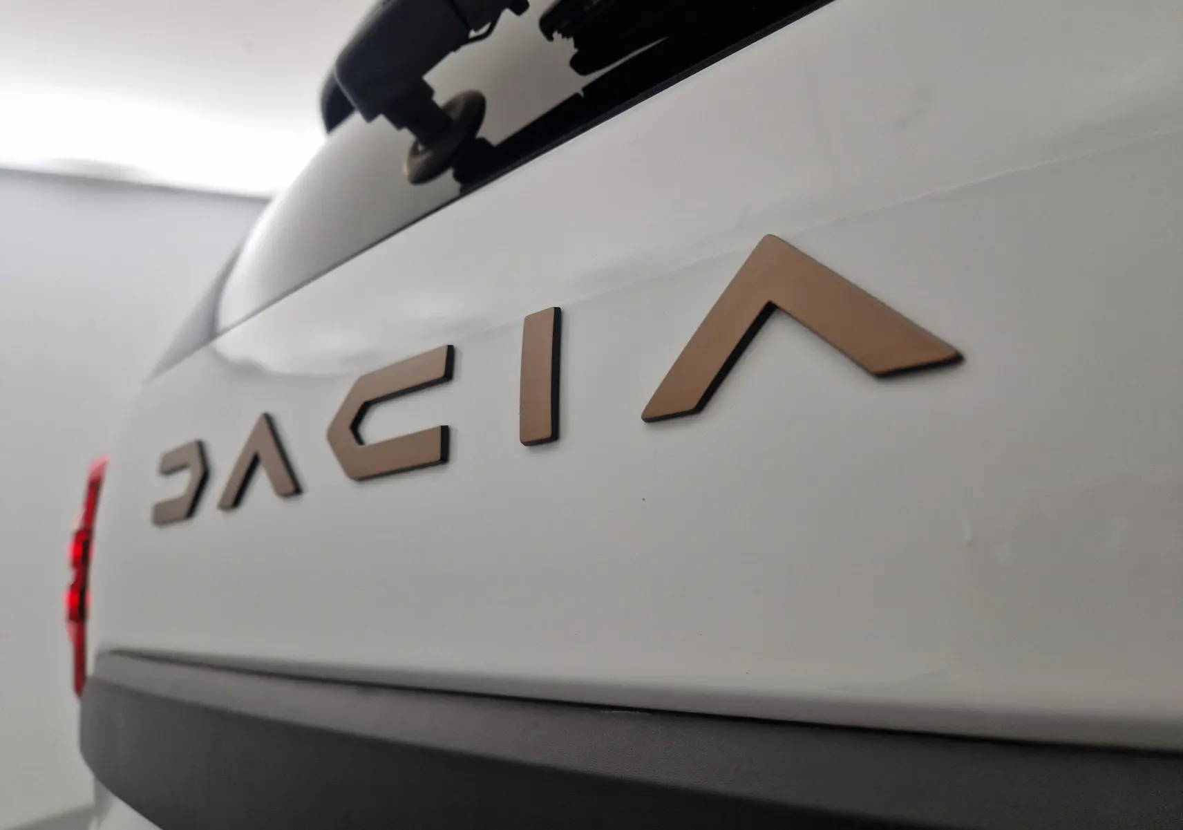 Gros plan sur le logo Dacia en relief bronze sur la partie arrière blanche du Duster 2024, avec feu arrière rouge partiel visible.