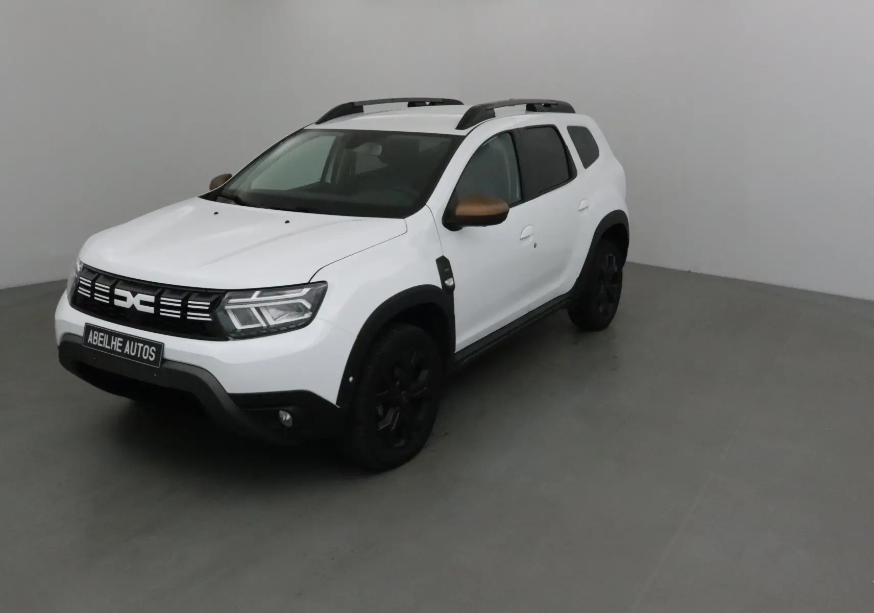 Dacia Duster 4x4 blanc en 3/4 avant droit avec coques de rétroviseurs bronze et jantes noires.