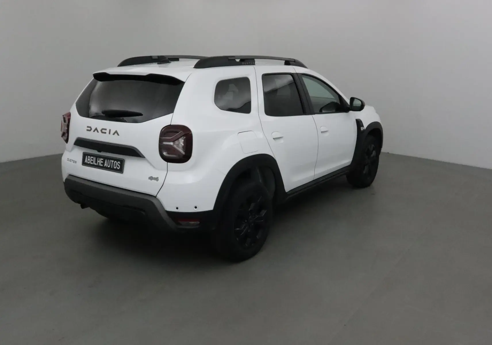 Vue 3/4 arrière droite d'un Dacia Duster blanc 4x4 2024 avec jantes noires et vitres teintées.