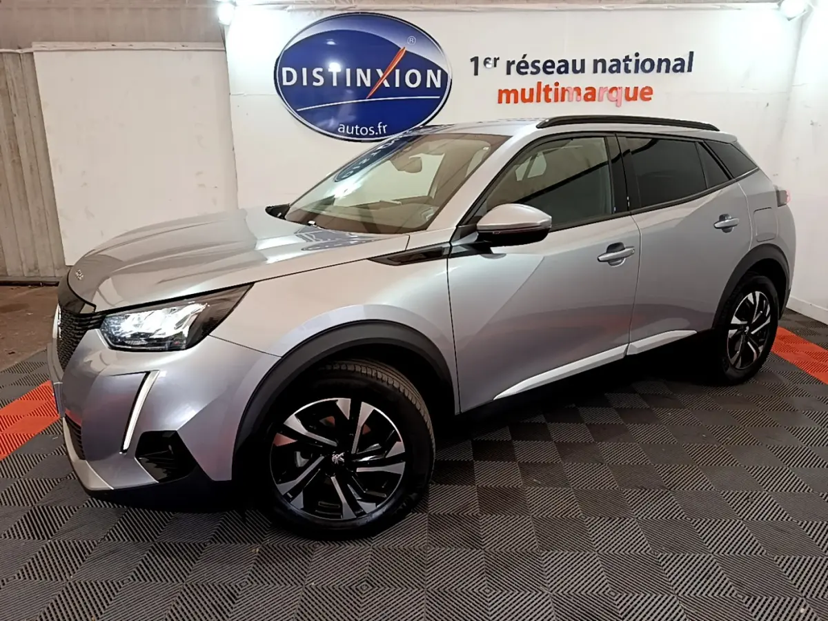 Peugeot 2008 gris clair en 3/4 avant droit, avec jantes noires et toit noir, stationné en intérieur showroom.