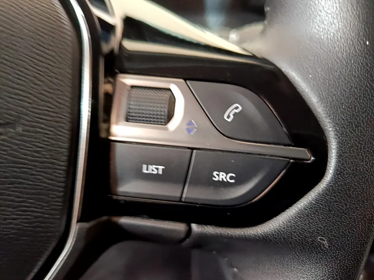 Gros plan sur les commandes du volant cuir noir du Peugeot 2008 gris clair, boutons appel et source audio visibles.
