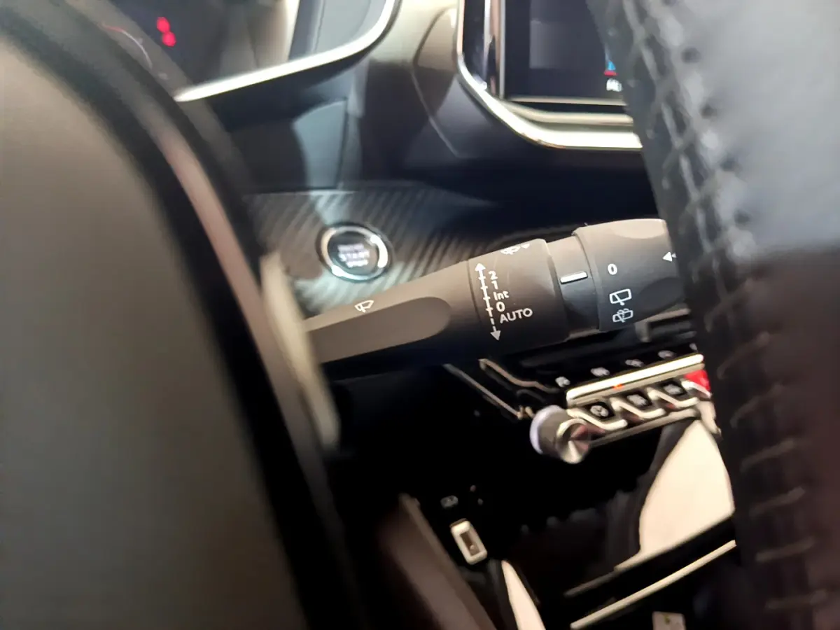 Gros plan sur la commande d'essuie-glace et bouton démarrage dans l'habitacle noir du Peugeot 2008 gris clair.