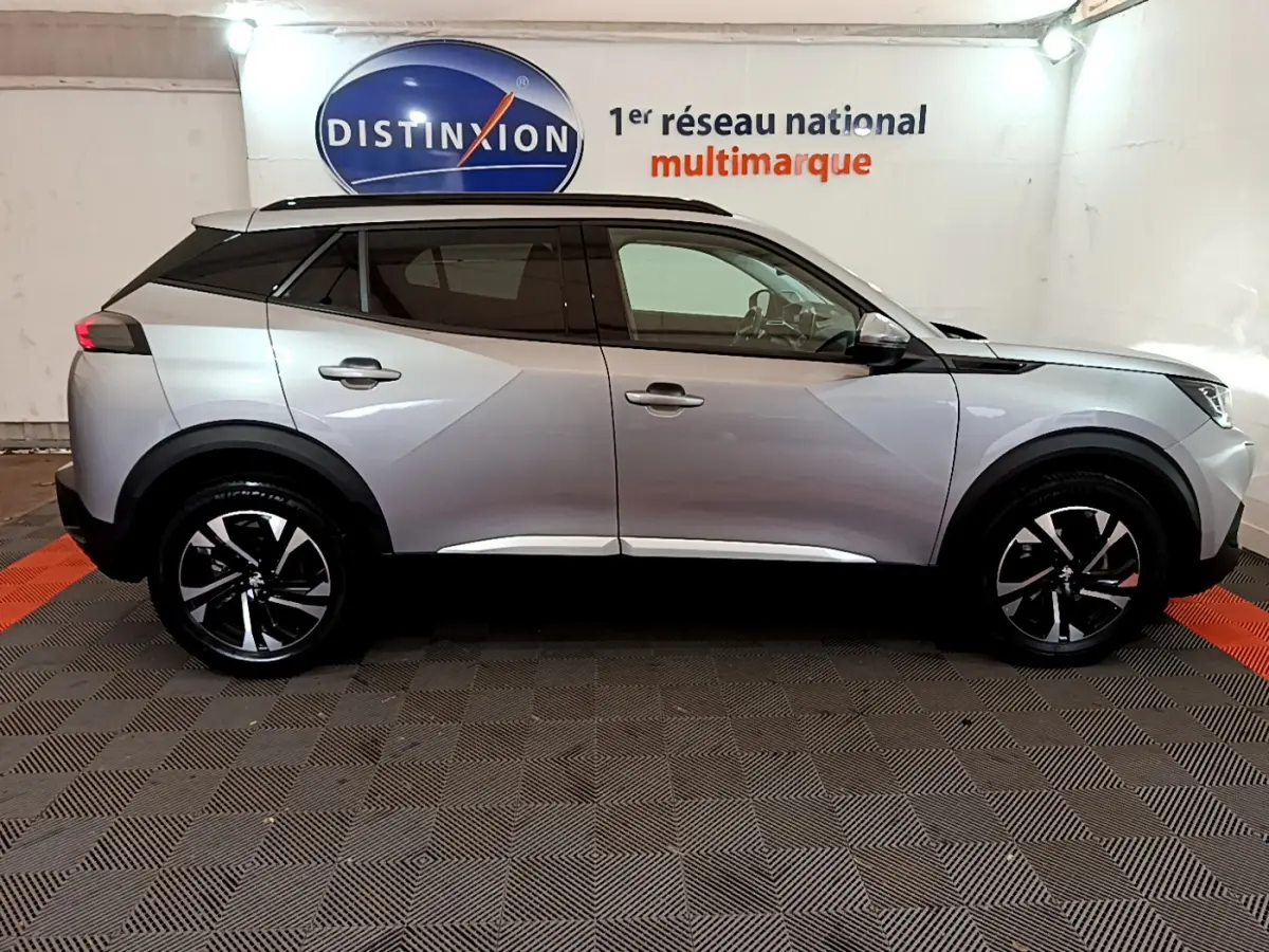 Profil côté droit d'un Peugeot 2008 gris clair 2021 avec jantes noires et toit noir en showroom.