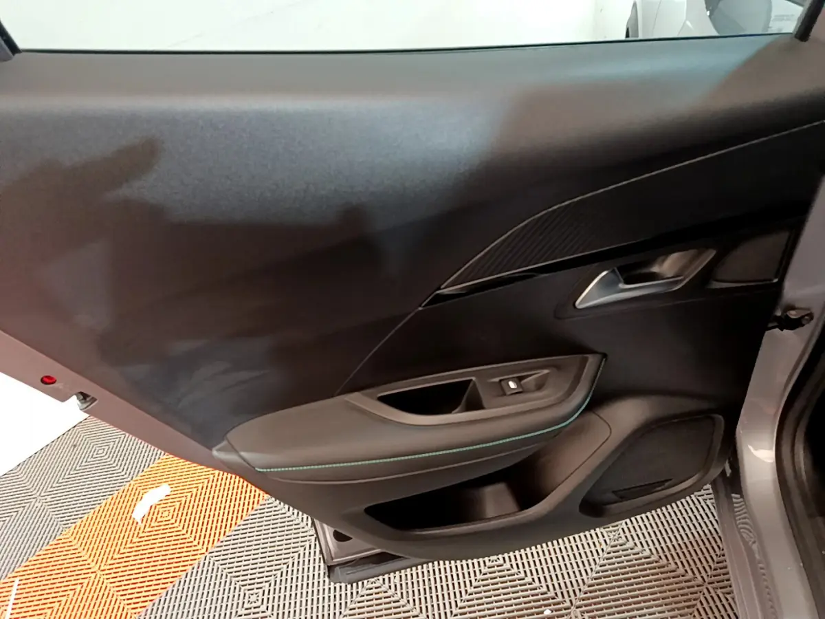 Vue intérieure de la porte côté gauche d'une Peugeot 2008 gris clair, avec garniture noire et surpiqûres bleues.