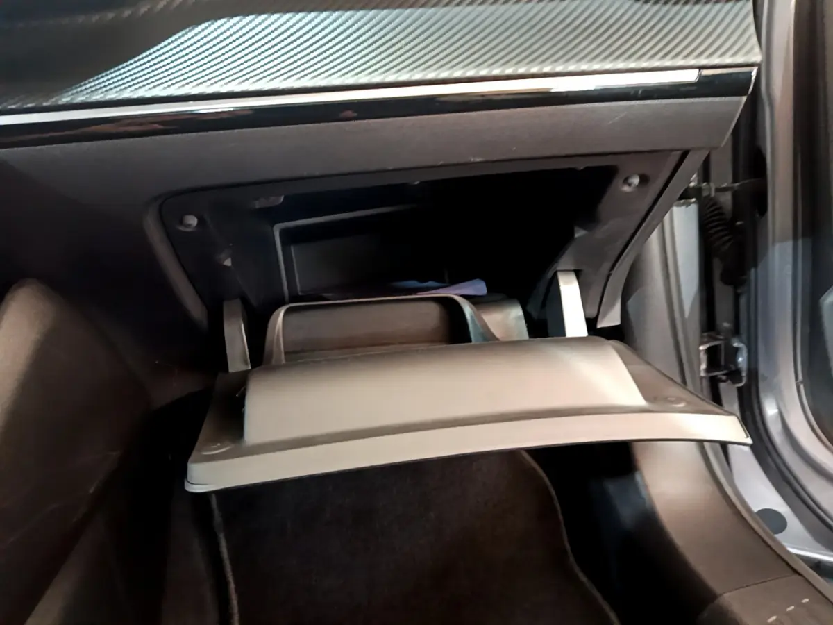 Gros plan sur la boîte à gants ouverte de la Peugeot 2008 gris clair, montrant l'intérieur noir et la portière côté droit entrouverte.