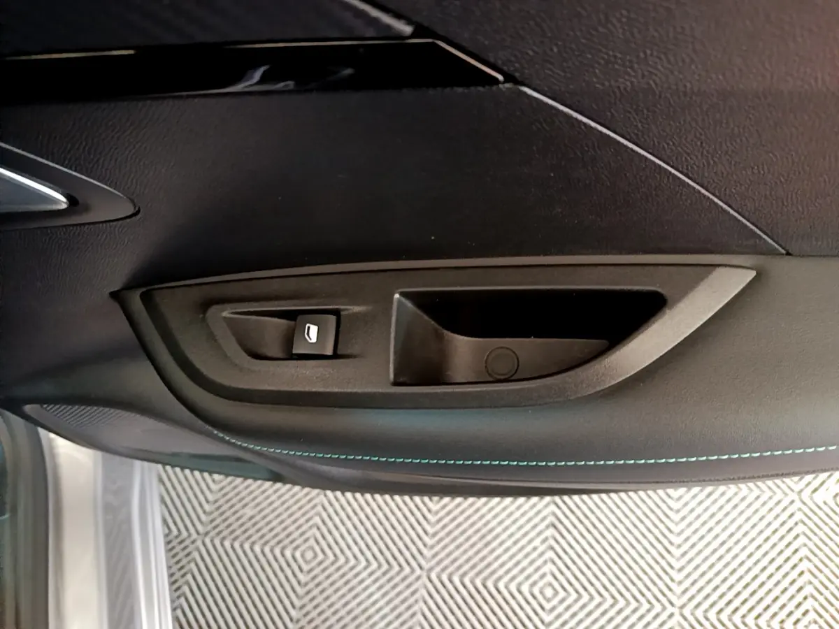 Détail de la poignée intérieure et commande de vitre côté gauche d'une Peugeot 2008 gris clair de 2021.