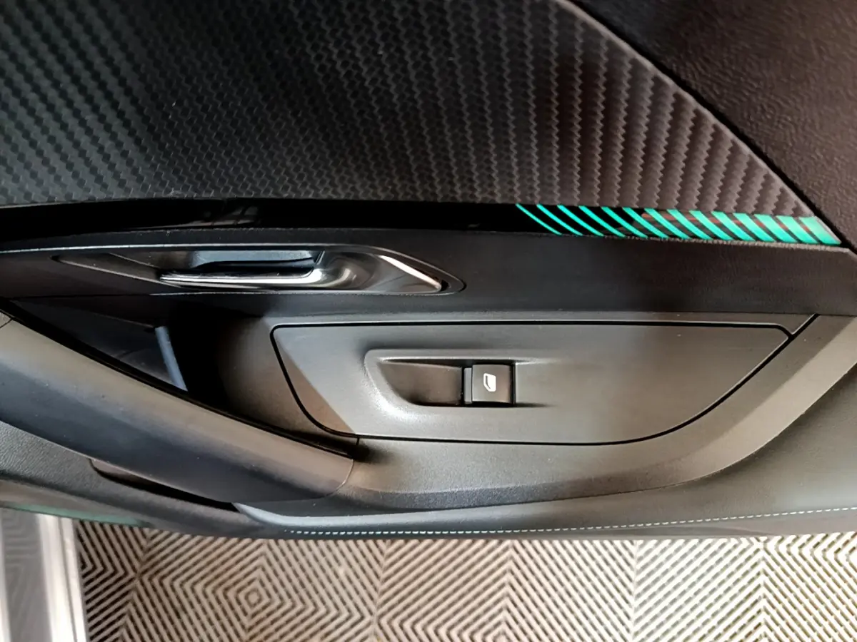 Détail de la porte côté gauche du Peugeot 2008 gris clair 2021 avec bouton de lève-vitre et insert décoratif noir à motifs.