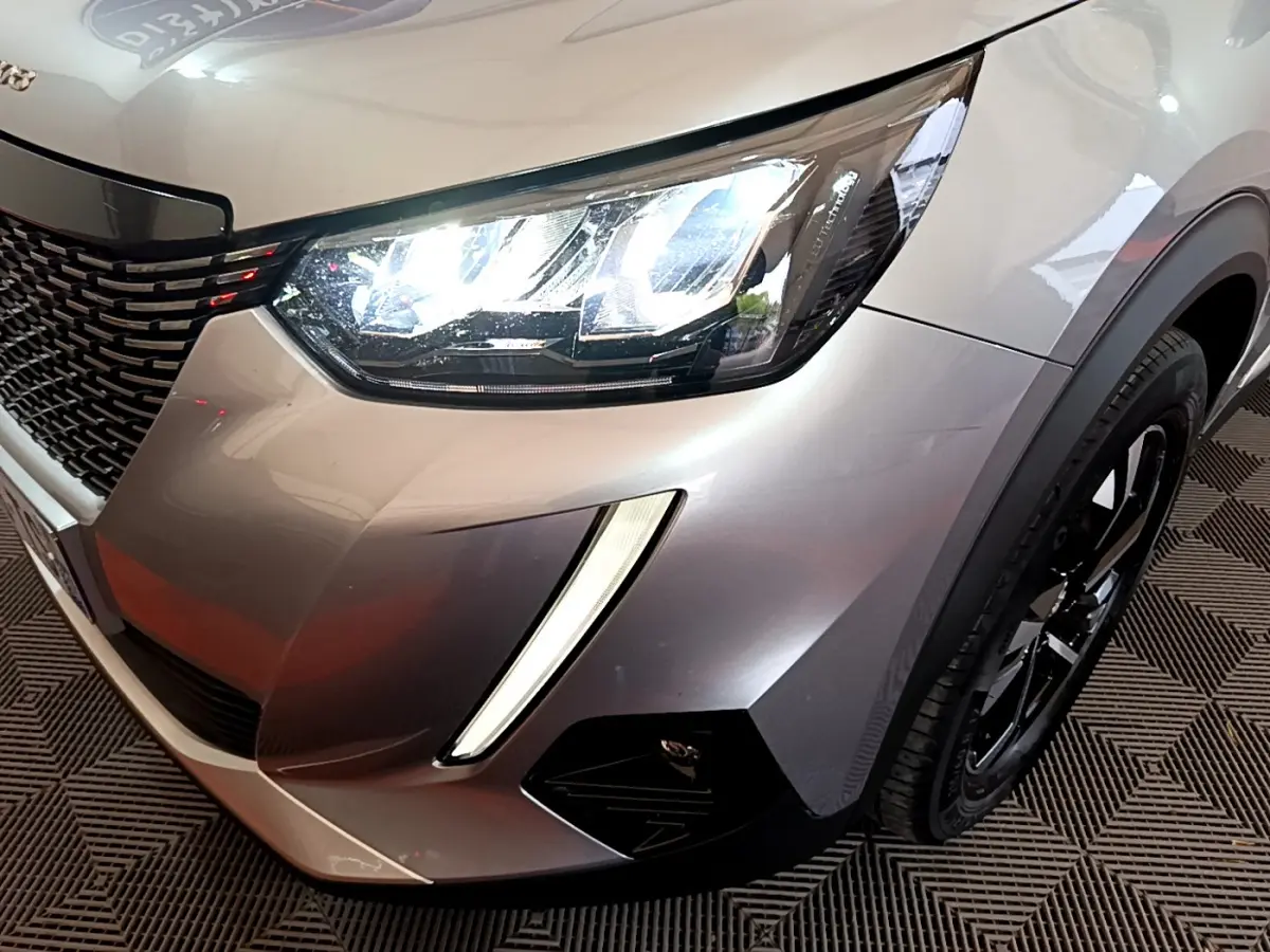 Gros plan sur l'avant droit gris clair du Peugeot 2008 2021, mettant en valeur le phare LED et la calandre noire.