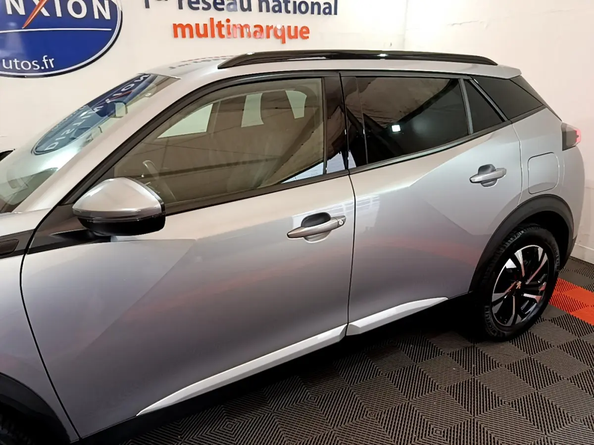 Profil côté gauche d'un Peugeot 2008 gris clair 2021 avec jantes noires et toit noir en intérieur showroom.