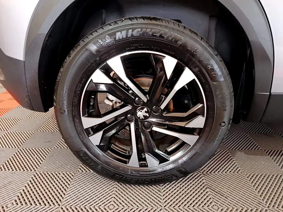 Gros plan sur la roue avant droite du Peugeot 2008 gris clair, avec jante alliage noire et argentée au design moderne.