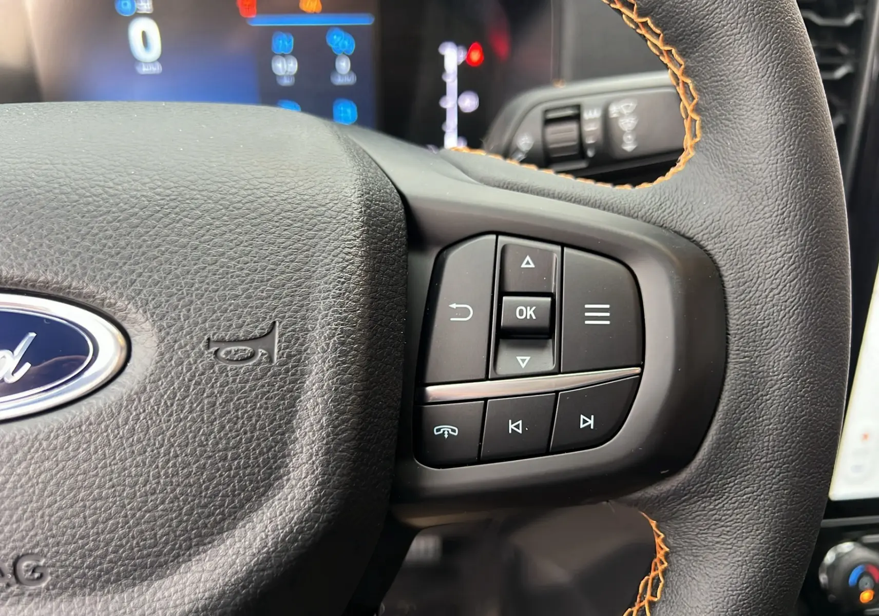 Gros plan sur le volant cuir noir avec surpiqûres orange du Ford Ranger 2026, boutons multifonctions visibles à droite.