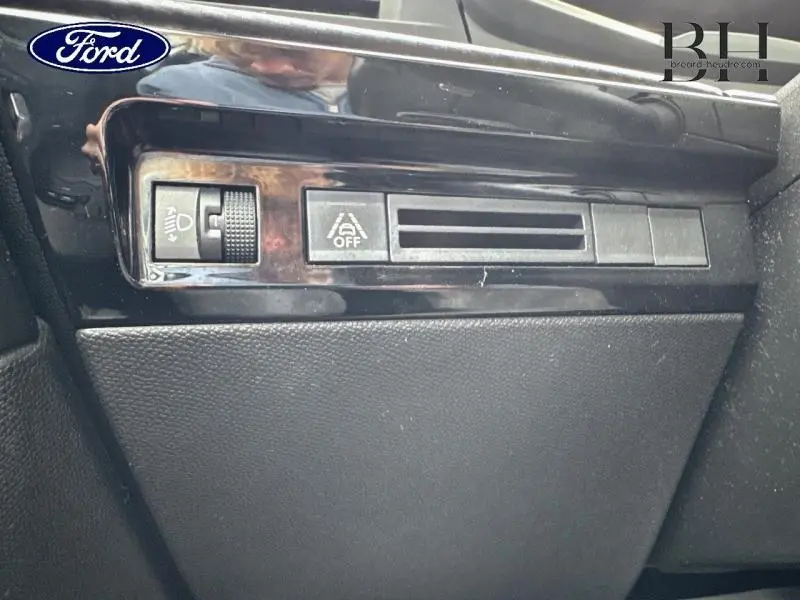 Détail intérieur montrant les commandes de réglage des phares et de désactivation du système start-stop sur un tableau de bord noir.