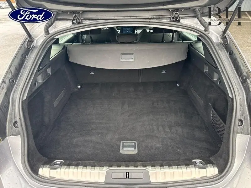 Vue arrière du coffre spacieux et propre d'un Peugeot 508 SW gris Platinium, avec cache-bagages et tapis noir.