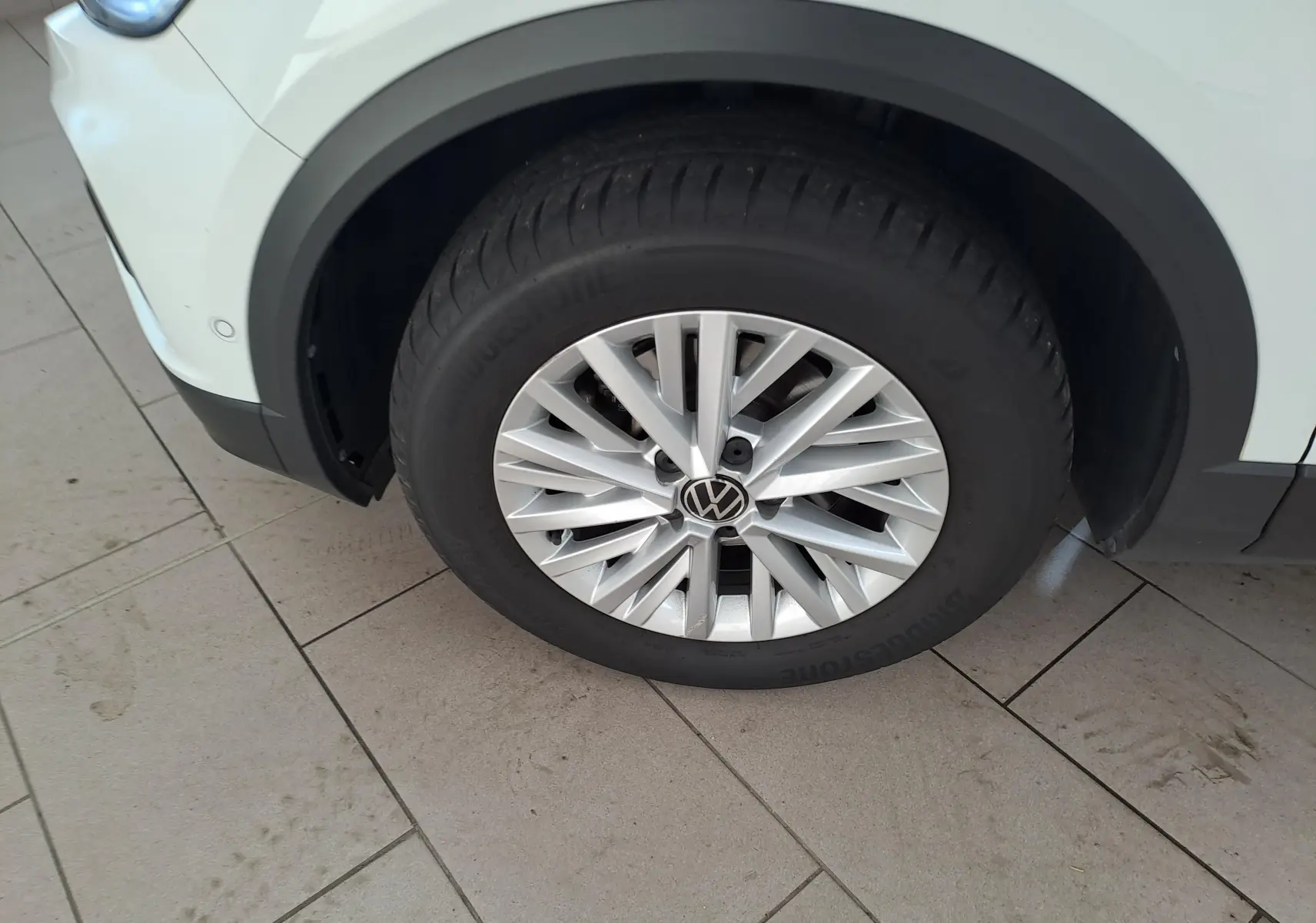 Gros plan sur la roue avant gauche du Volkswagen T-Roc blanc pur avec jante alliage et toit noir visible en partie.