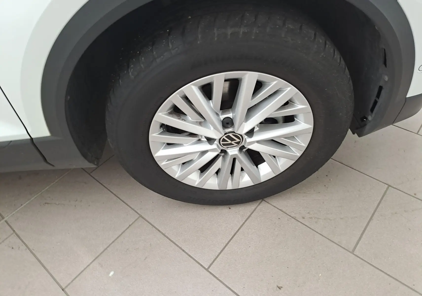 Gros plan sur la roue avant gauche du Volkswagen T-Roc blanc pur avec jante alliage et logo VW au centre.