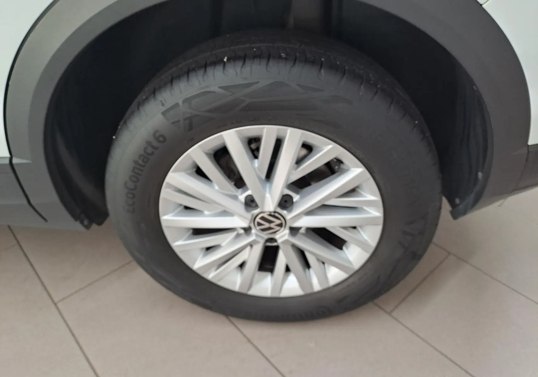 Gros plan sur la roue avant gauche du Volkswagen T-Roc blanc pur avec jante alliage et logo VW au centre.