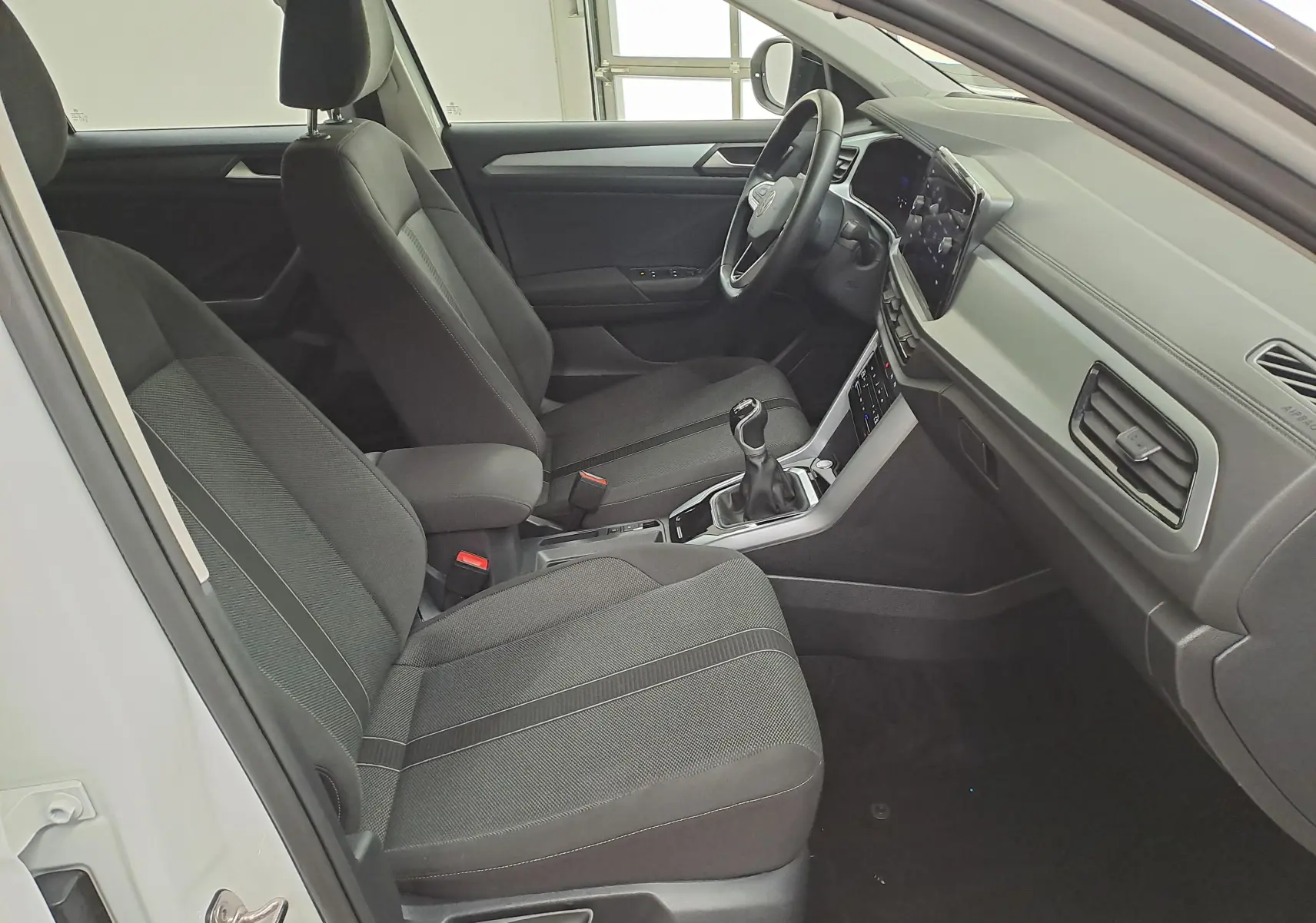 Vue intérieure côté conducteur du Volkswagen T-Roc 2022 blanc, montrant les sièges noirs et la console avec boîte manuelle.