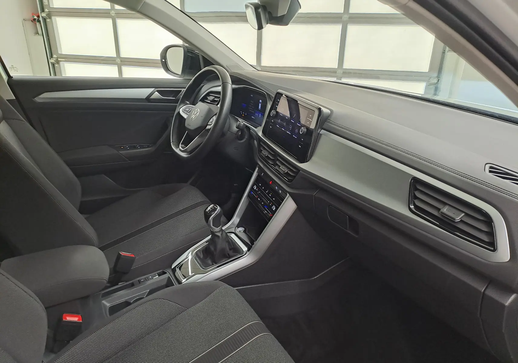Vue intérieure côté conducteur du Volkswagen T-Roc 2022, tableau de bord moderne avec écran tactile et volant multifonction noir.